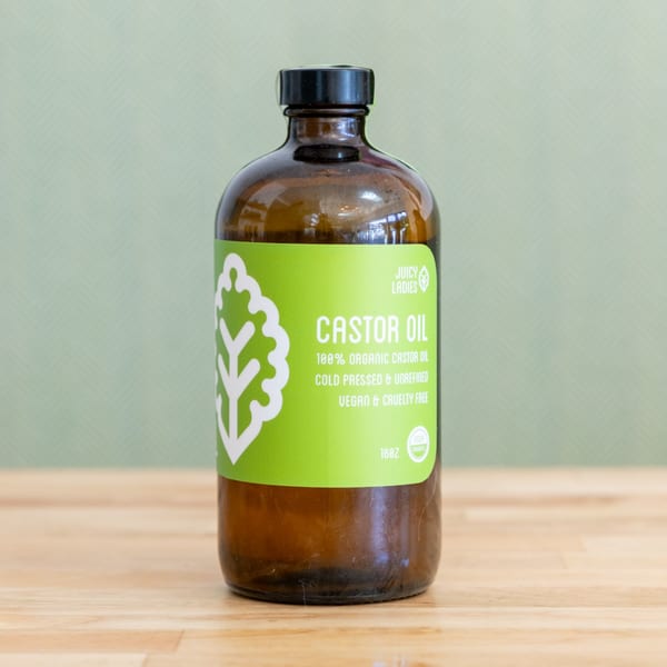 Amber glass bottle of Juicy Ladies organic castor oil with a bright green label on a wooden surface.