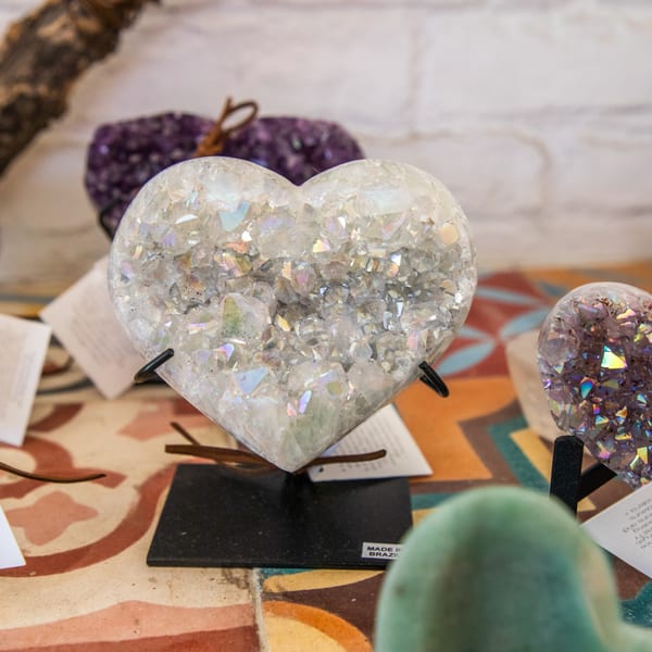 A heart-shaped crystal geode with iridescent facets sits on a patterned table.