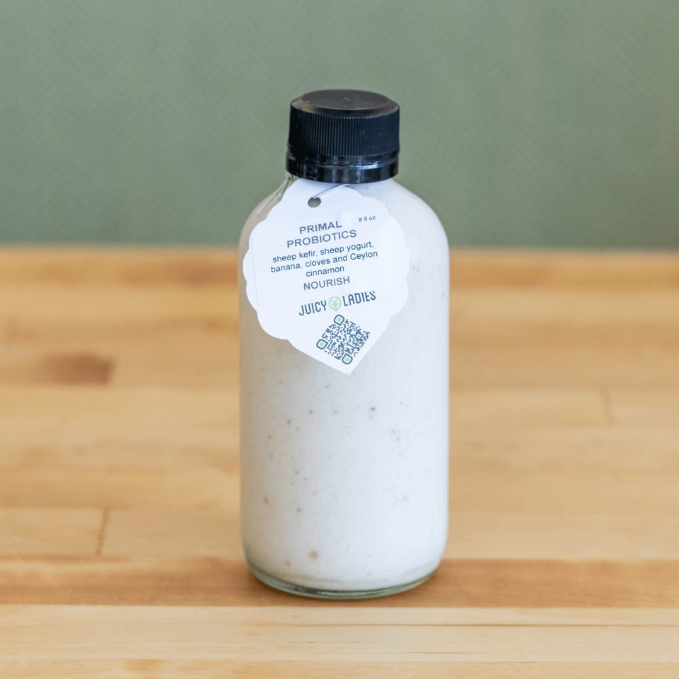 Bottle of Juicy Ladies Primal Probiotics, a creamy sheep kefir drink, standing on a wooden table.
