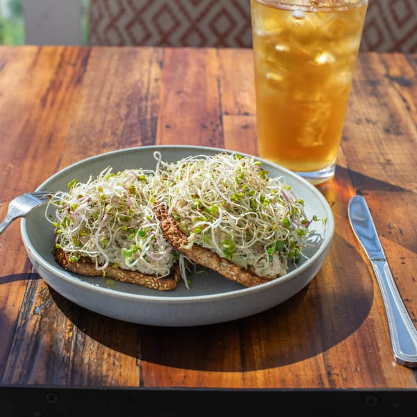Two avocado toasts topped with sprouts on a gray plate, with an iced tea on a wooden table.