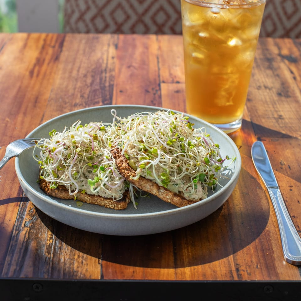 Two avocado toasts topped with sprouts on a gray plate, with an iced tea on a wooden table.