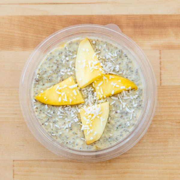 Overhead view of chia pudding topped with mango slices and shredded coconut in a clear bowl on a wooden table.