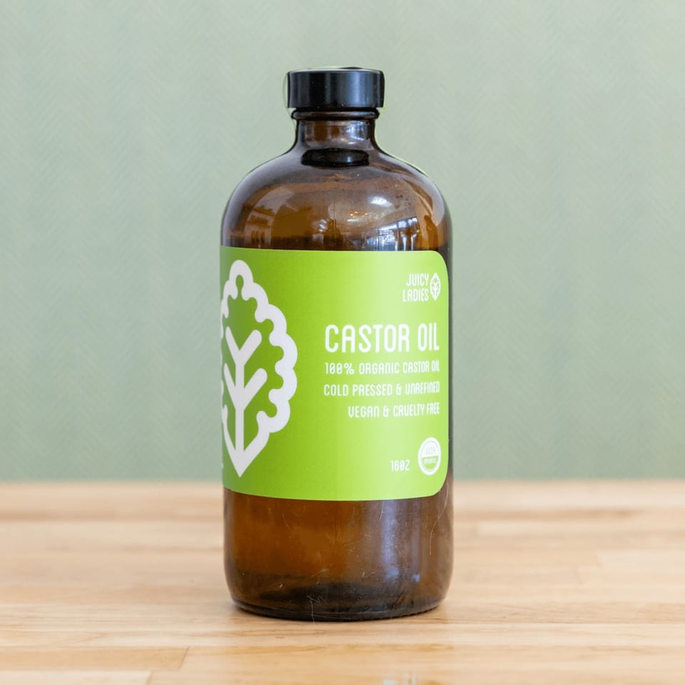 Amber bottle of Juicy Ladies organic castor oil with a bright green label on a wooden table.