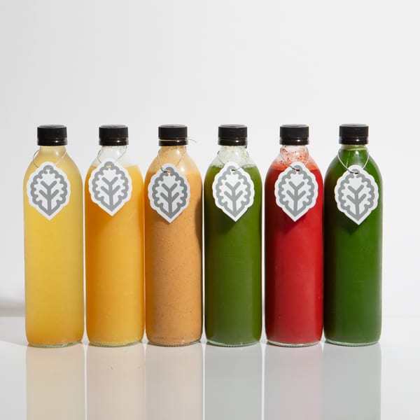 Six colorful bottles of Juicy Ladies healthy juices, each with a leaf-shaped tag, on a white surface.