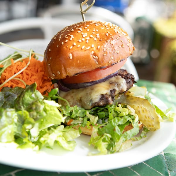 A Juicy Ladies burger with melted cheese, lettuce, tomato, onion, and pickles, served with shredded carrots.