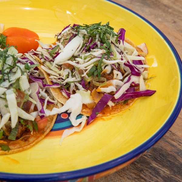 Two healthy tacos with shredded cabbage, purple cabbage, and herbs on a yellow plate.