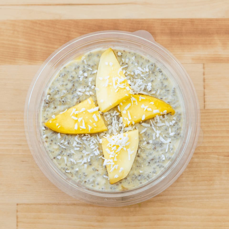 Chia seed pudding topped with mango slices and shredded coconut in a clear bowl on a wooden table.