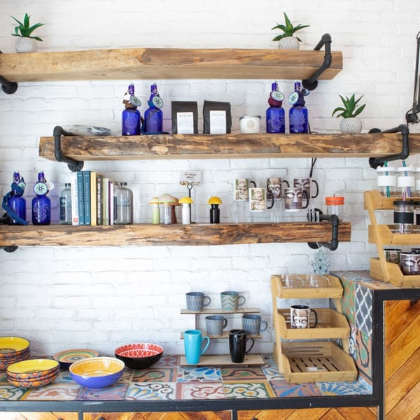 Rustic wooden shelves on a white brick wall display Juicy Ladies products, mugs, and cookbooks.
